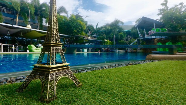 A miniature Eiffel Tower in a grassy area with a pool and palm trees in the background. - Momento Resort (Pattaya)
