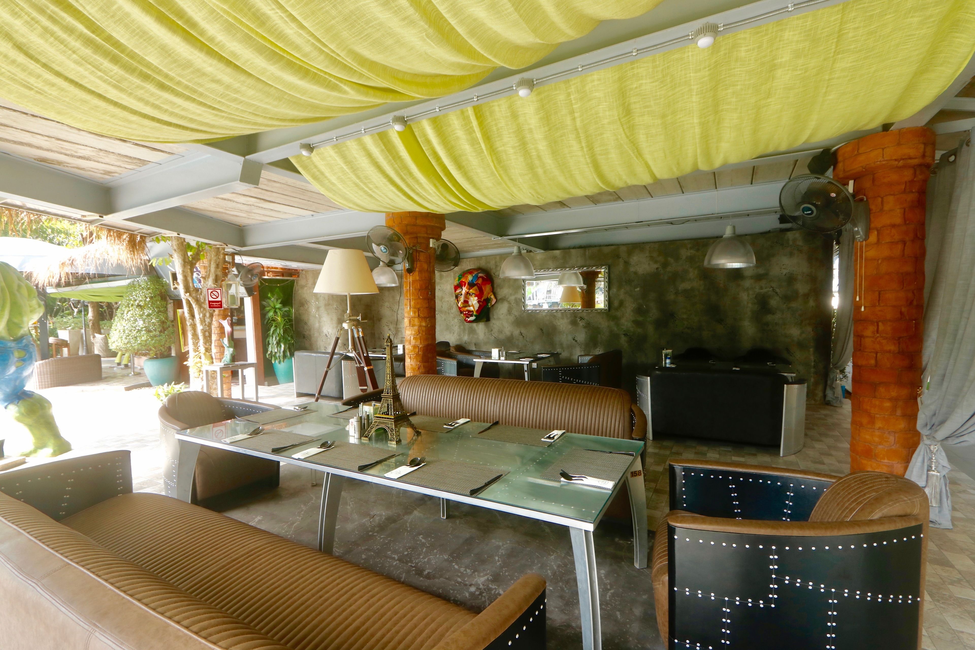 A restaurant with a glass table, cushioned seating, and a green canopy.