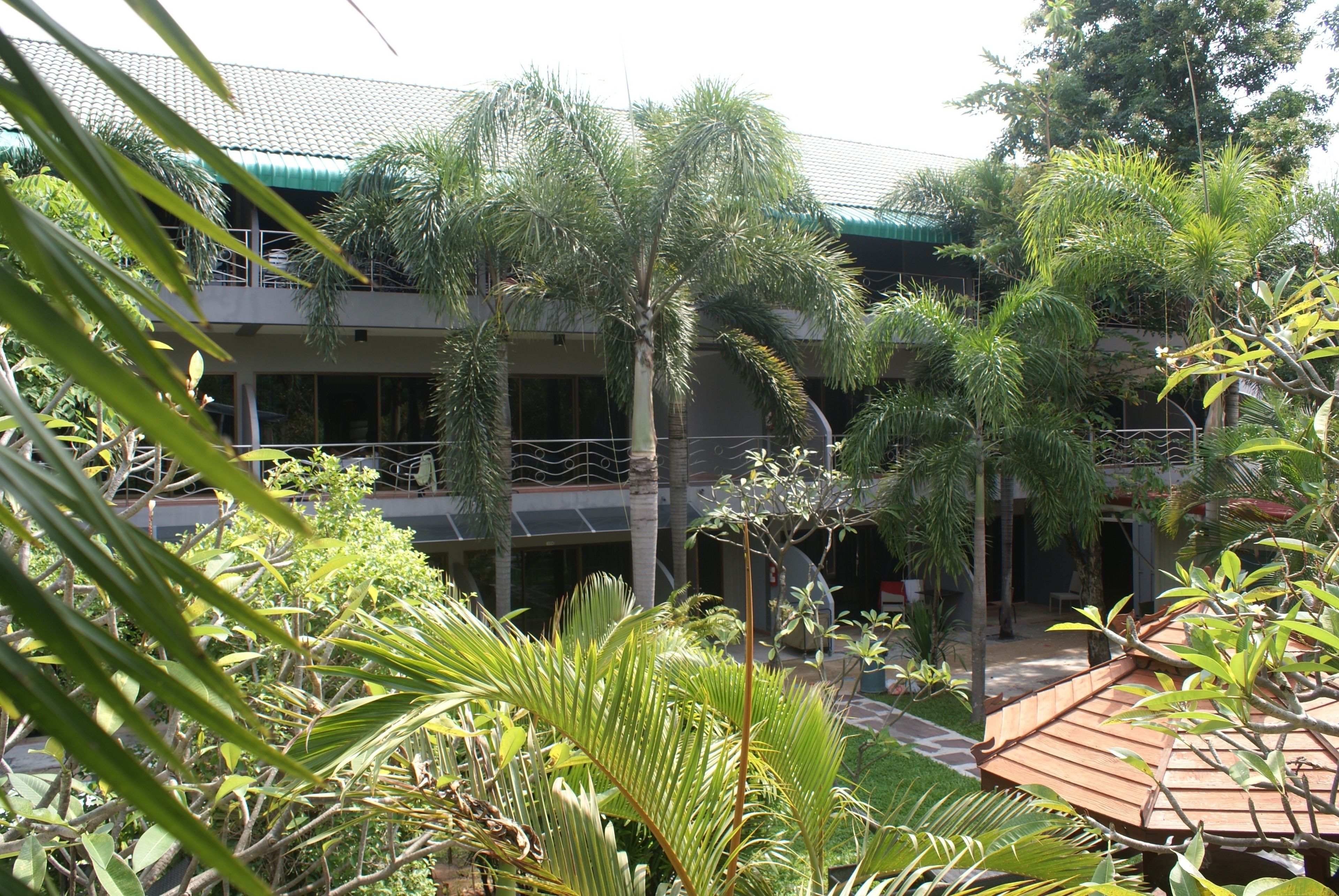 A building with a green roof and multiple balconies surrounded by lush greenery.
