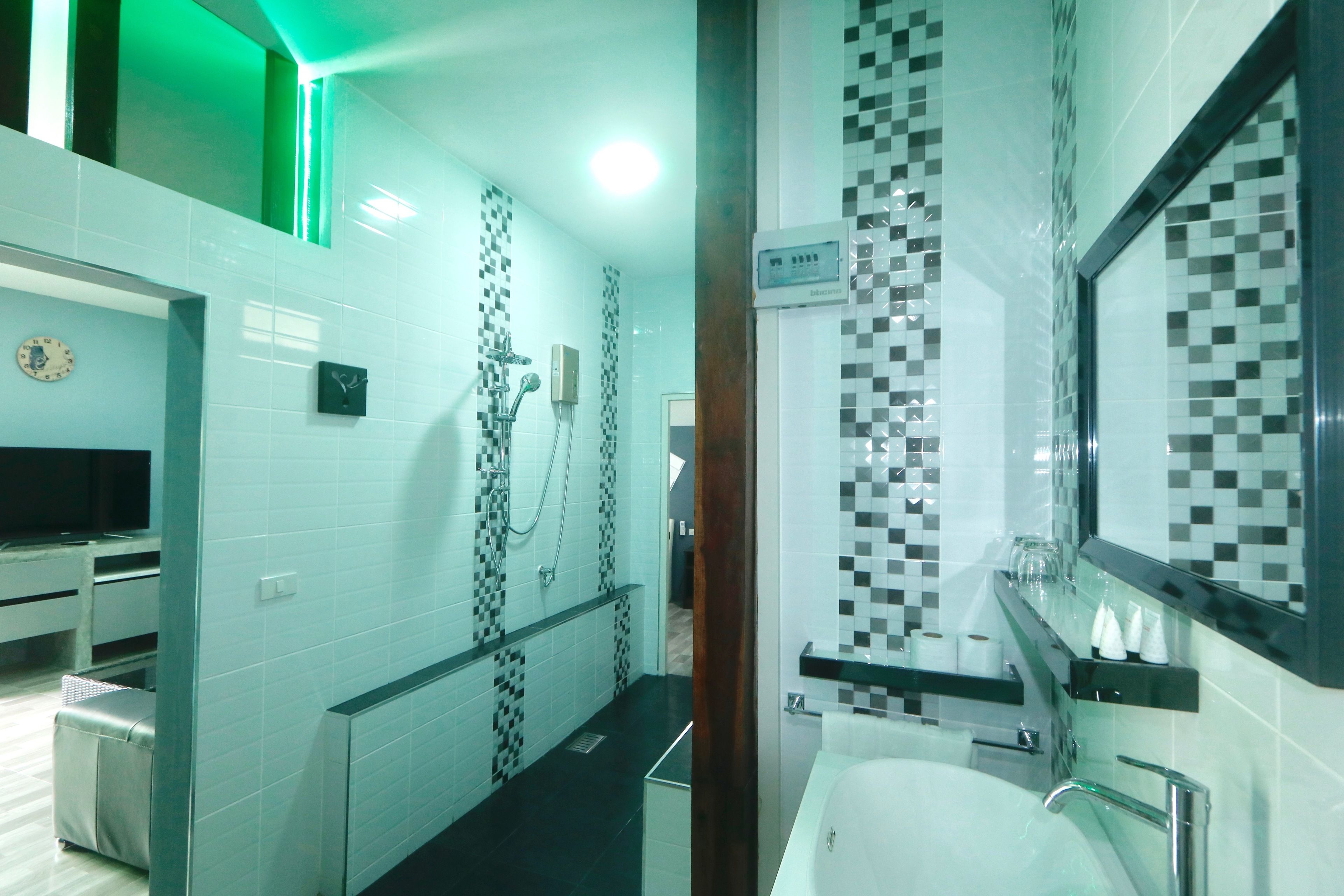 A modern bathroom with a shower, a sink, and a mirror. There is a clock on the wall and a television in the corner.
