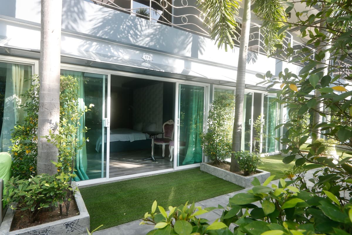 A modern hotel room with a glass door leading to a balcony, a small seating area, and a neatly landscaped garden.