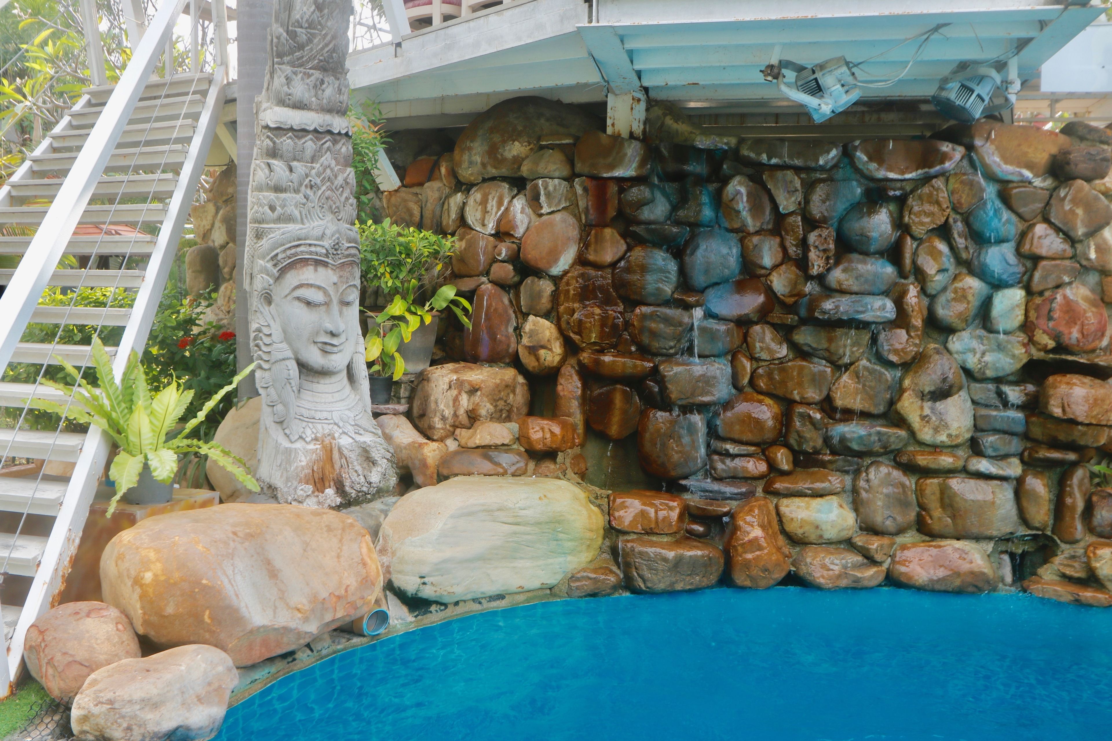 A stone wall with a water feature, a large rock, and a statue.