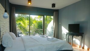 A hotel room with a large bed, a TV on a small table, and a view of palm trees through the window. - Momento Resort (Pattaya)