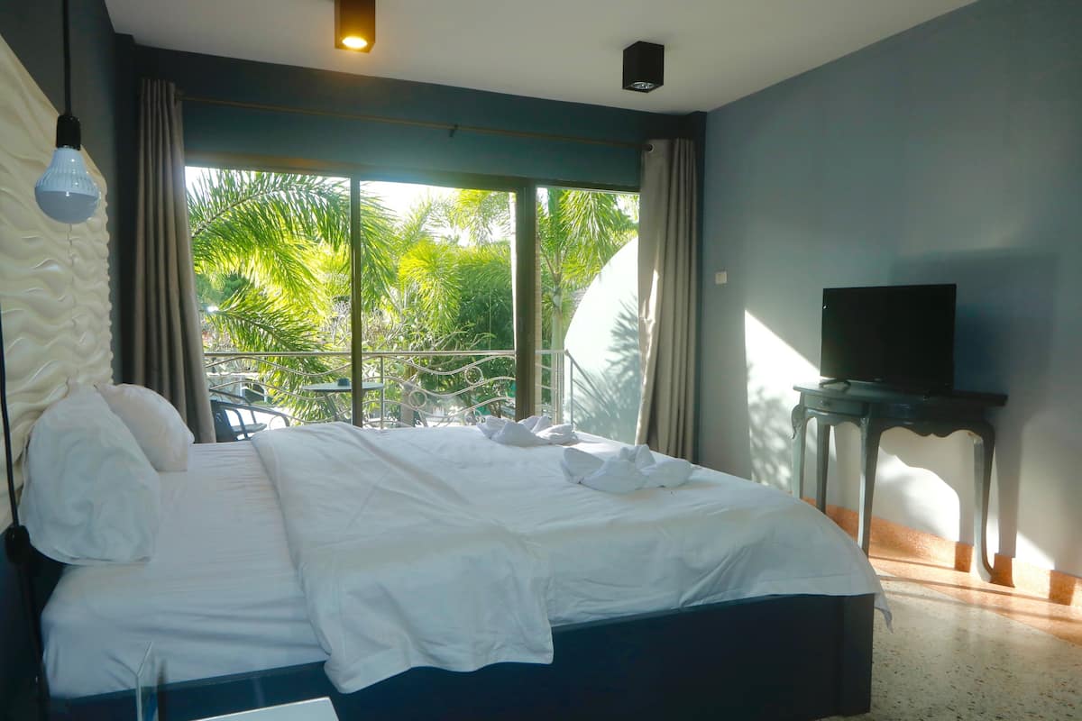 A hotel room with a large bed, a TV on a small table, and a view of palm trees through the window.