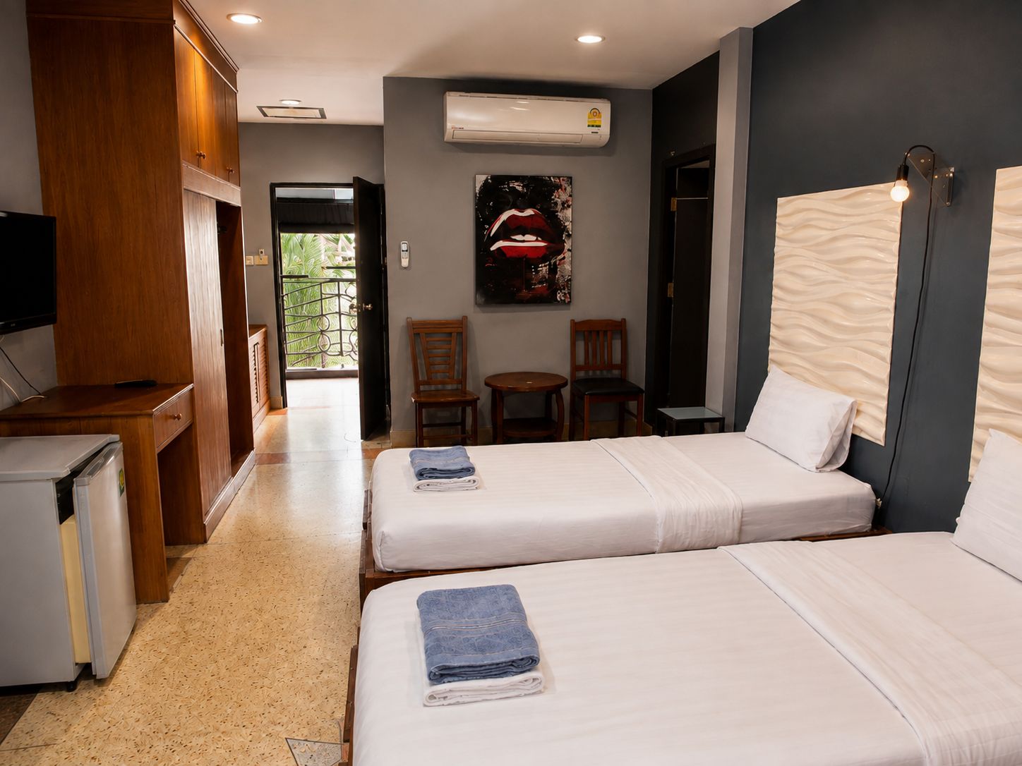 A hotel room with two beds, a desk, a television, and a door leading to a balcony.