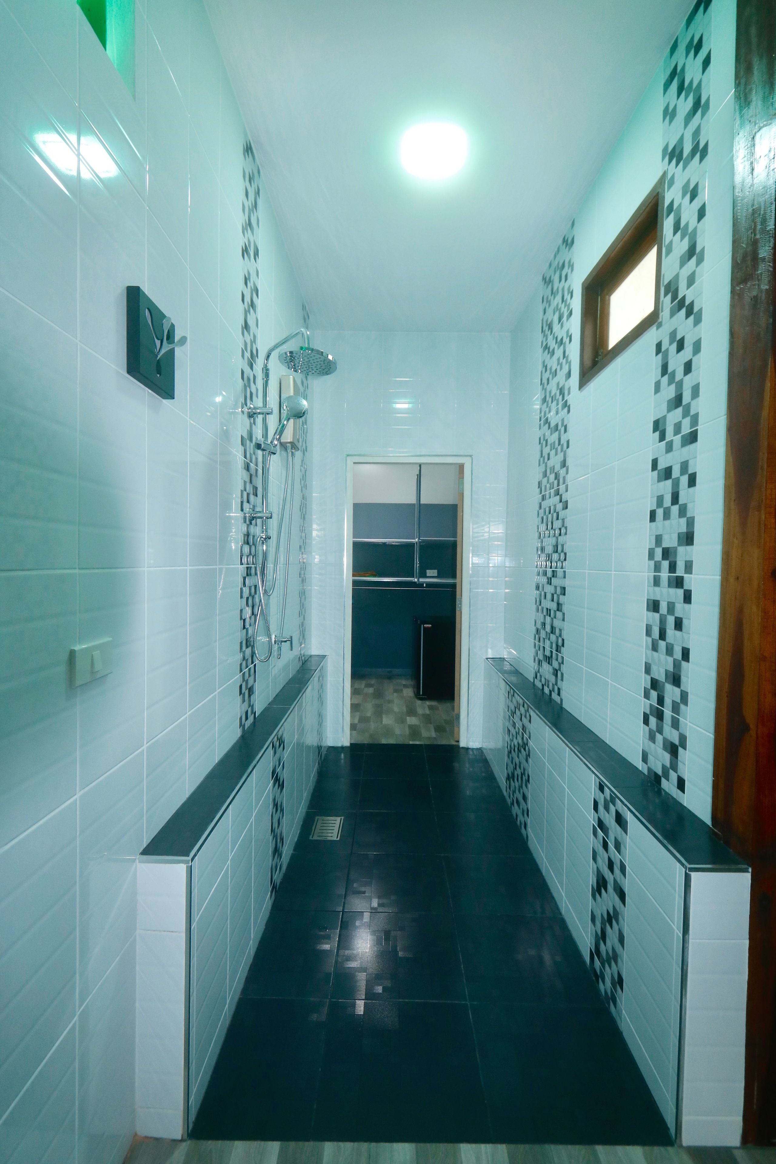A narrow hallway with tiled walls and a black floor, leading to a room with a door.