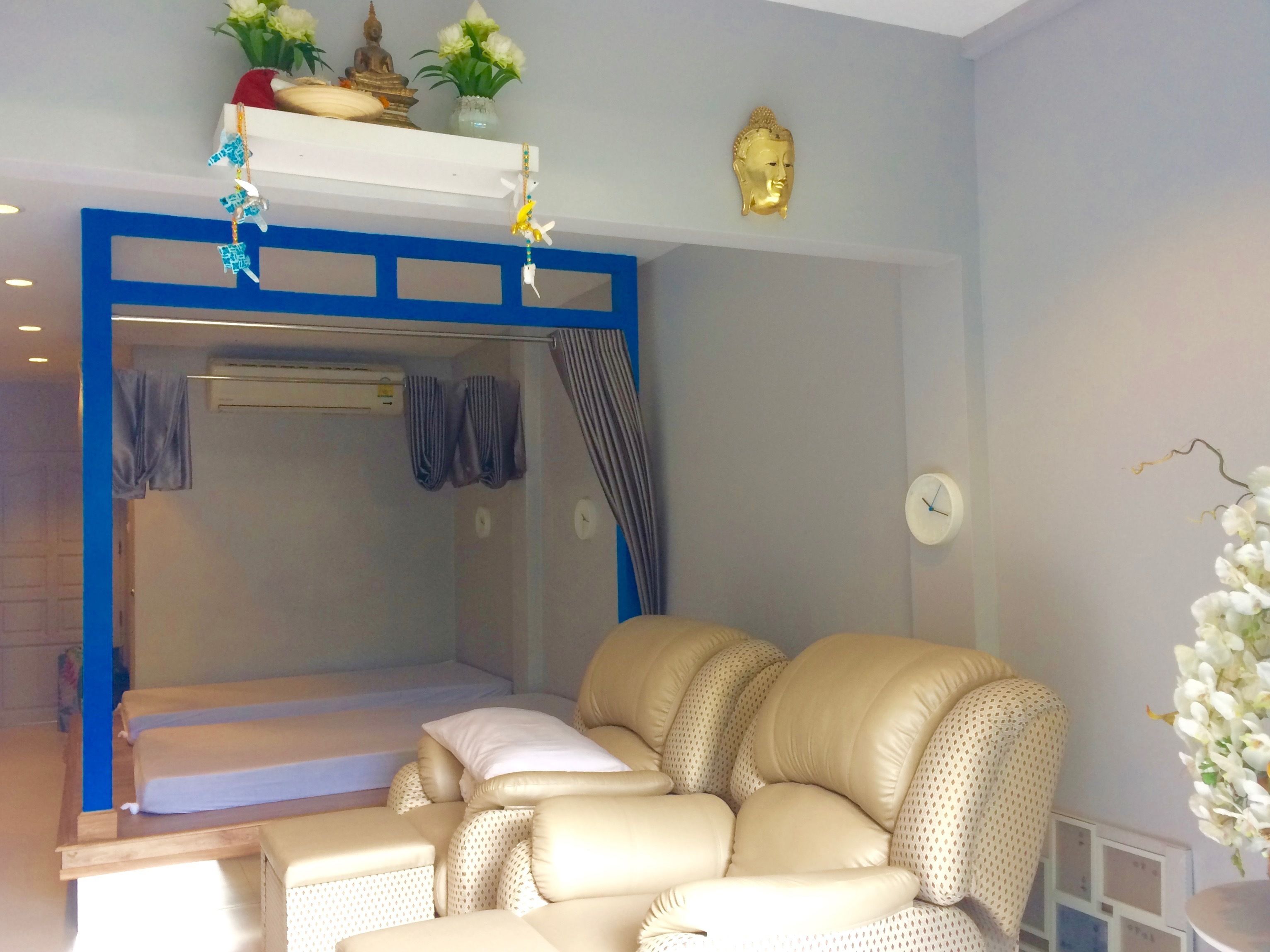 A room with a bed, a sofa, a small table, a wall clock, and a Buddha statue.