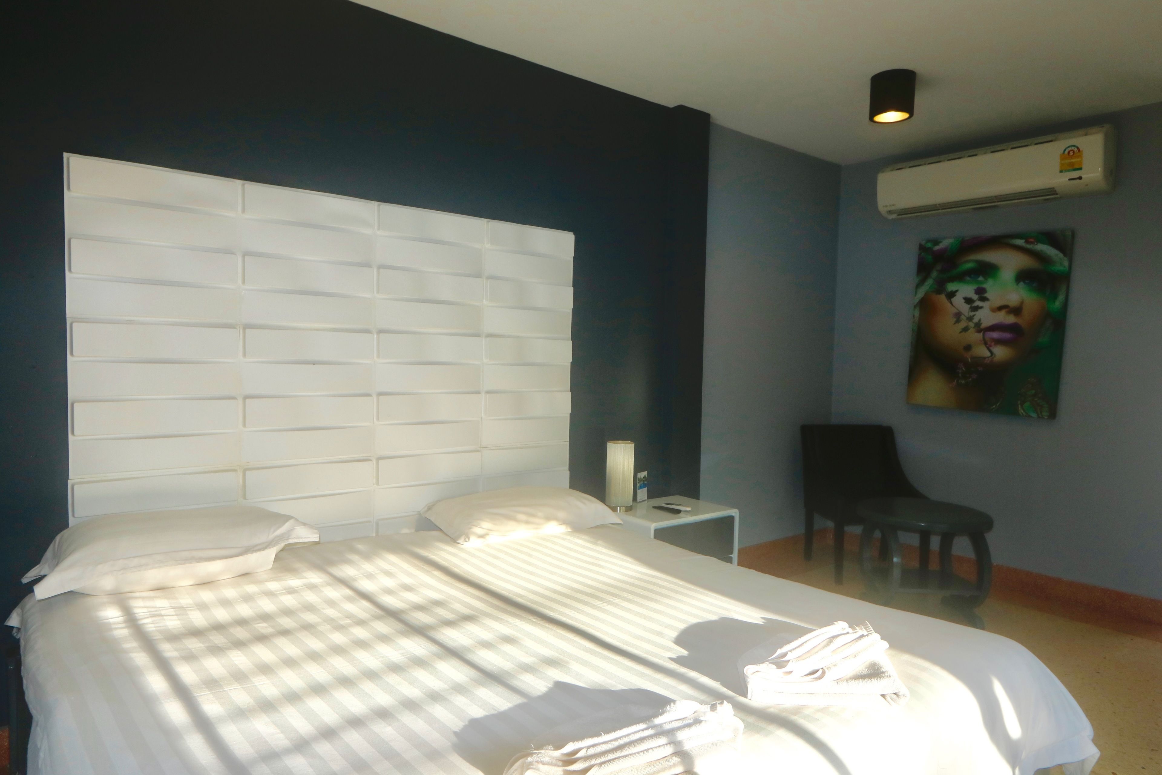 A bedroom with a large bed, a nightstand, a chair, and an air conditioning unit on the wall.