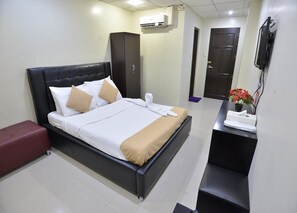 Habitación de hotel ordenada con cama, escritorio, armario y aire acondicionado.