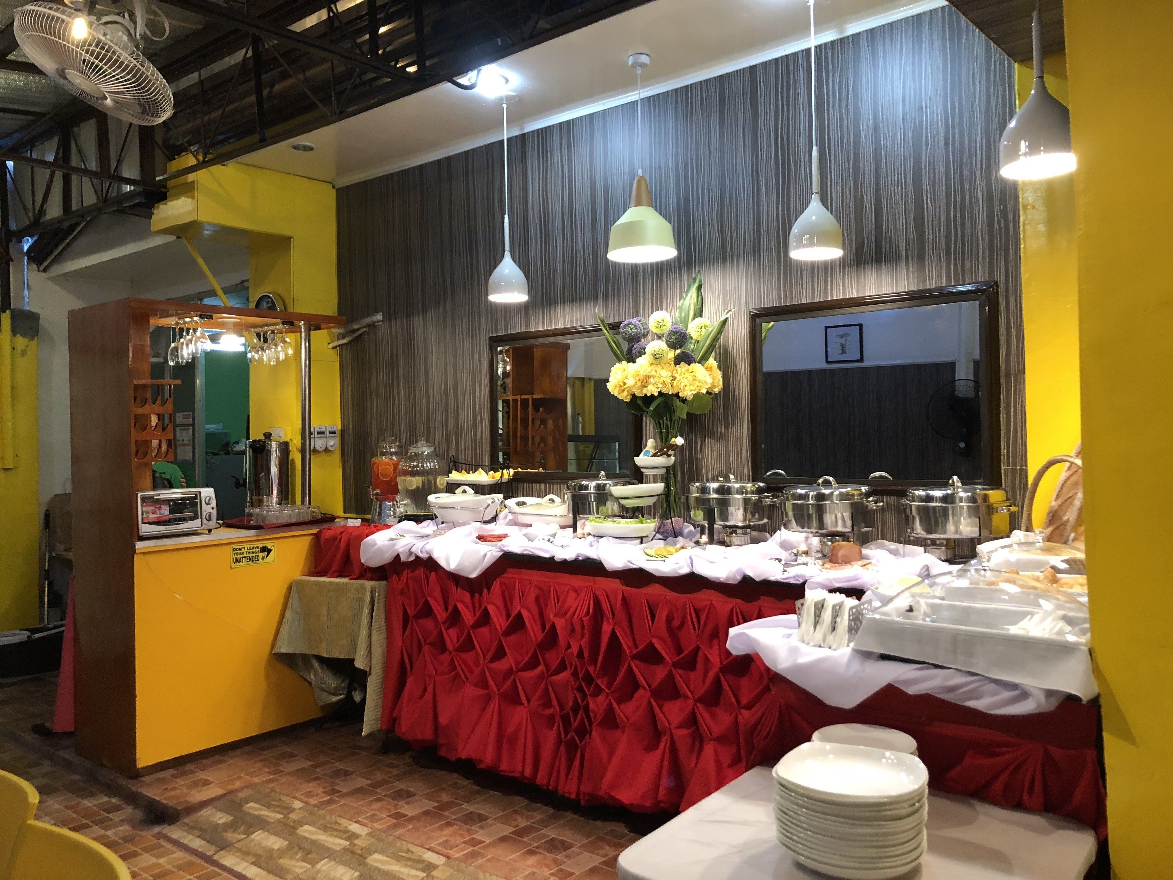 A buffet setup with a red tablecloth, multiple serving stations, and a mirror on the wall.