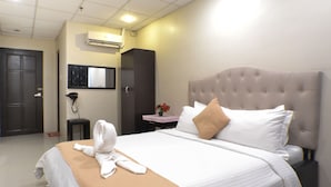 Habitació d'hotel amb un llit gran, una taula de nit, un escriptori petit, un aparell d'aire condicionat i una porta.