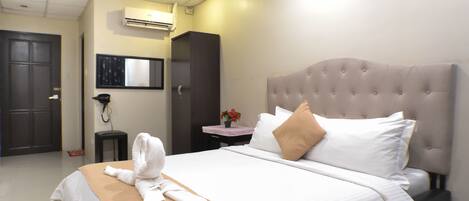 Habitación de hotel con una cama grande, una mesita de noche, un escritorio pequeño, un equipo de aire acondicionado y una puerta.