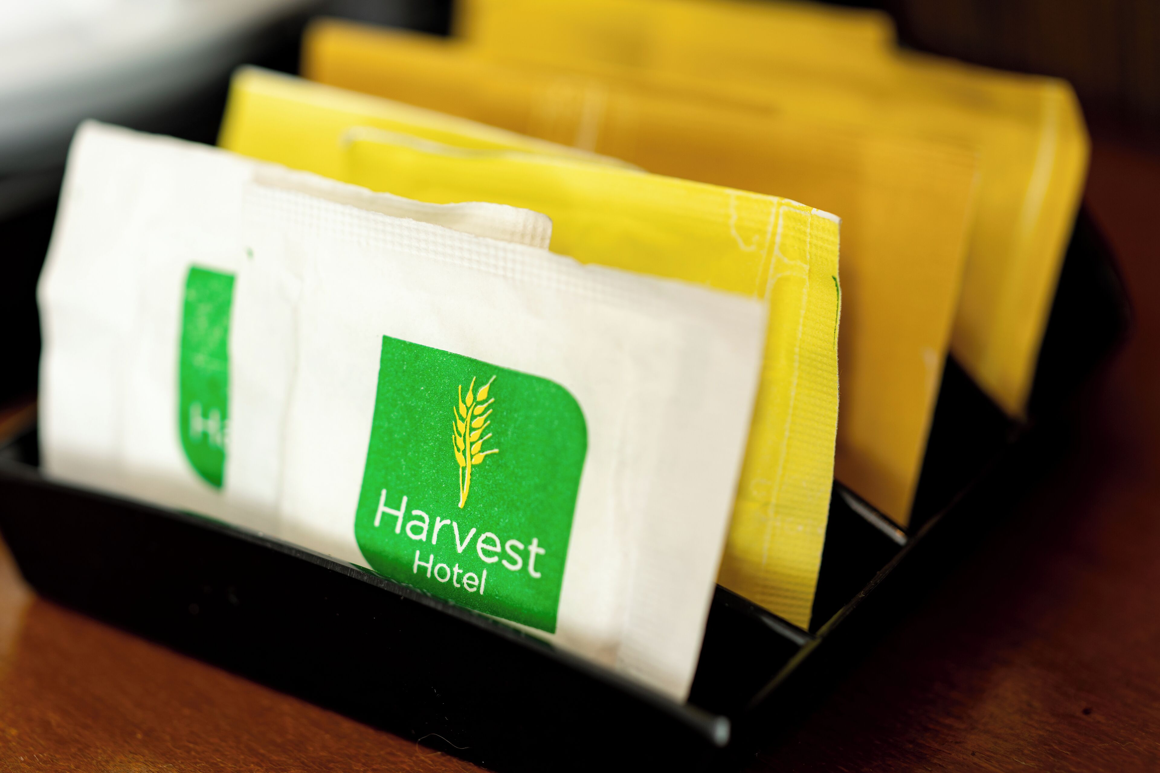 A hotel room with a black tray holding a white pillow and a yellow pillow with a green logo.