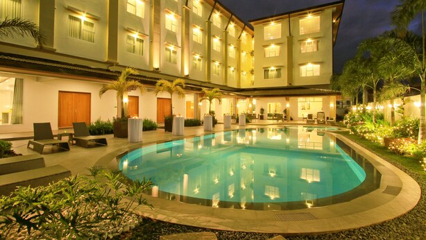A hotel with a swimming pool, lounge chairs, and a well-lit exterior at night.