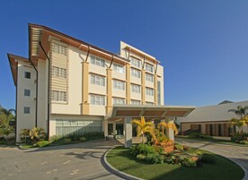 Un hotel moderno con una entrada central, varios pisos y un jardín ajardinado.