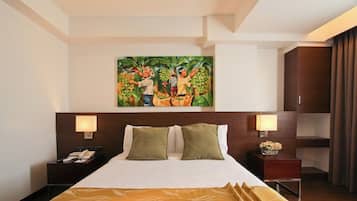 A hotel room with a large bed, two bedside lamps, a nightstand with a phone, and a painting of people holding fruit on the wall.