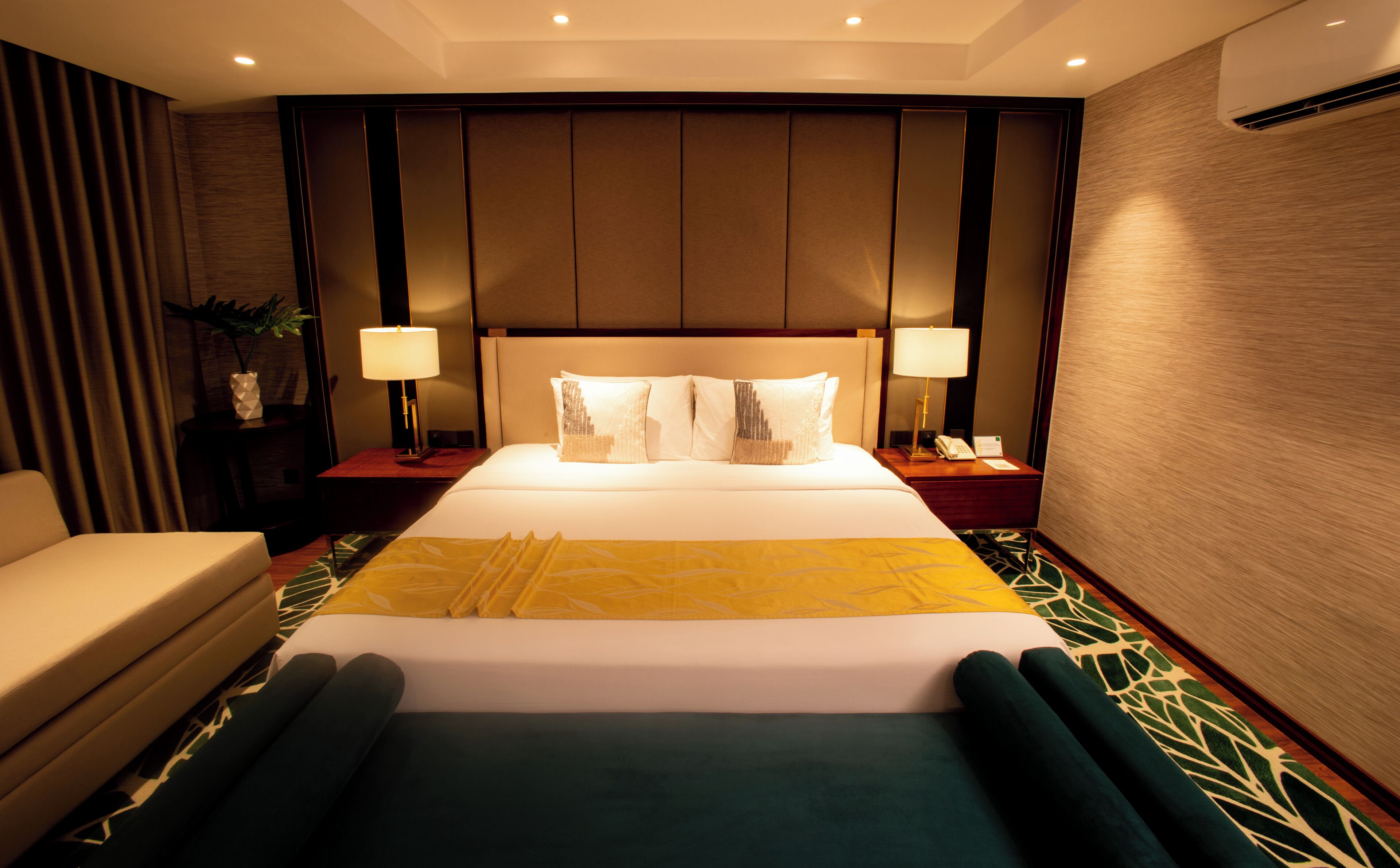 Habitación de hotel con una cama grande, dos mesitas de noche con lámparas, una silla y una planta en maceta.