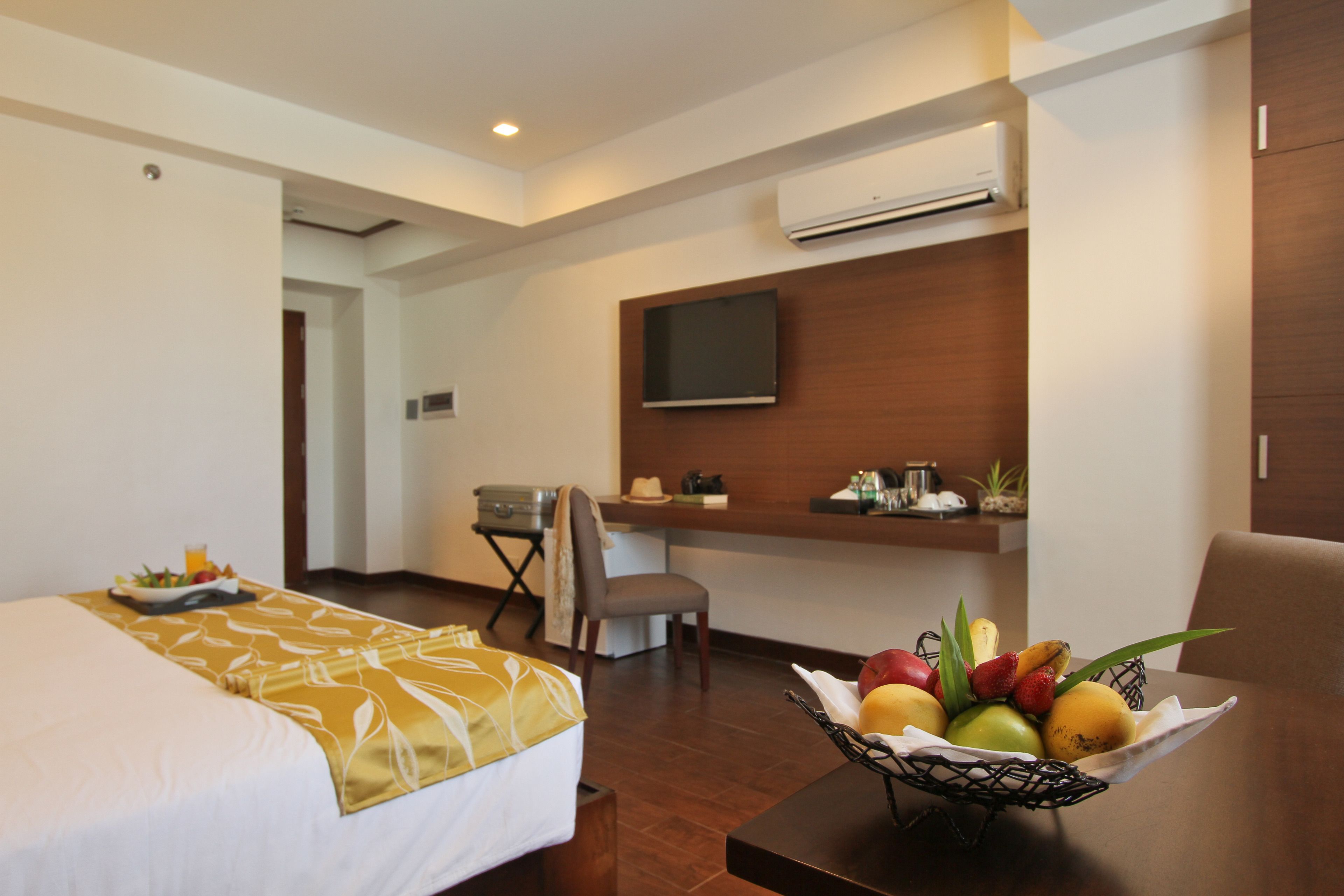 Une chambre d’hôtel comprenant un lit, un bureau avec un téléviseur à écran plat, un panier de fruits et un appareil de climatisation.