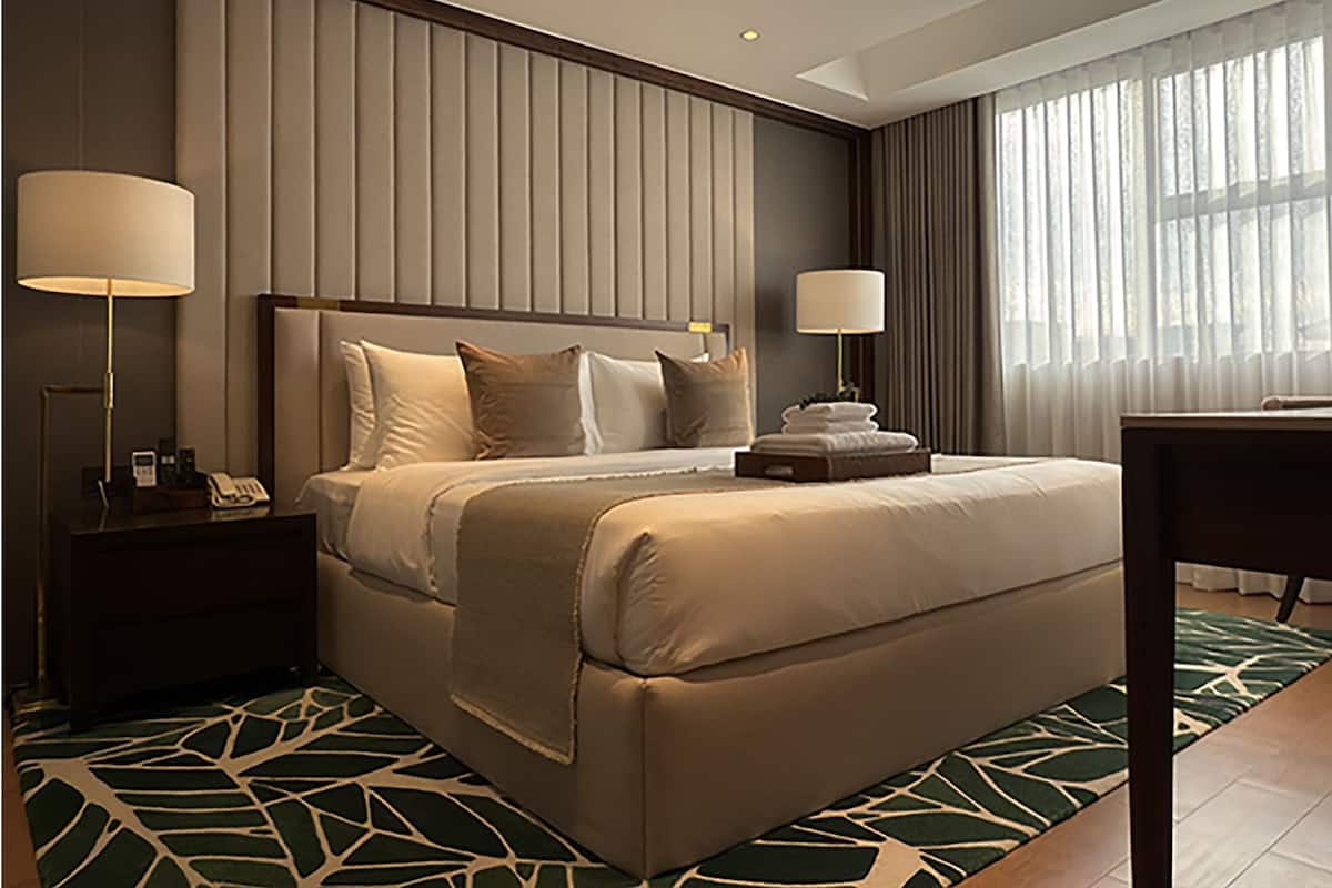 A hotel room with a large bed, two bedside tables, a desk, and a window with curtains.