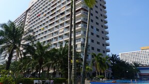 Un hôtel de grande hauteur doté de nombreux balcons, d’un espace piscine et de palmiers.