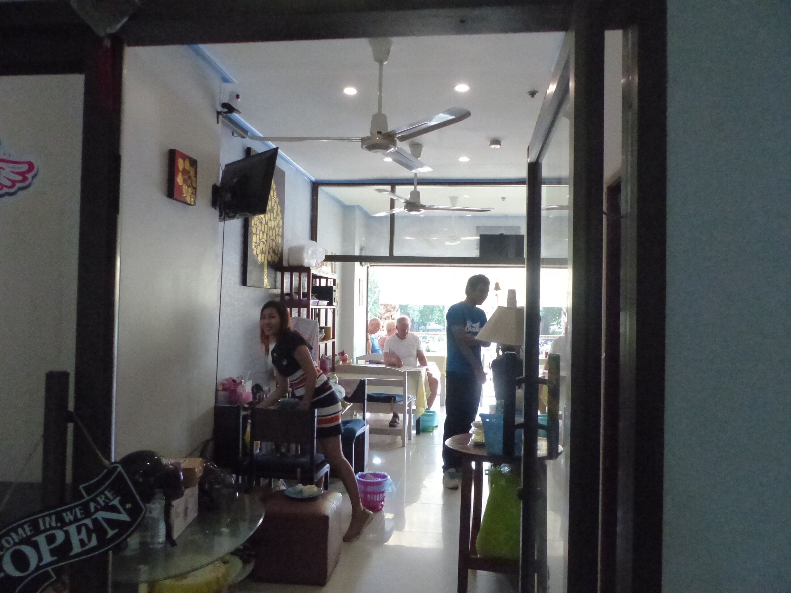 An interior view of a restaurant with a dining area, kitchen, and a person standing near the kitchen counter.