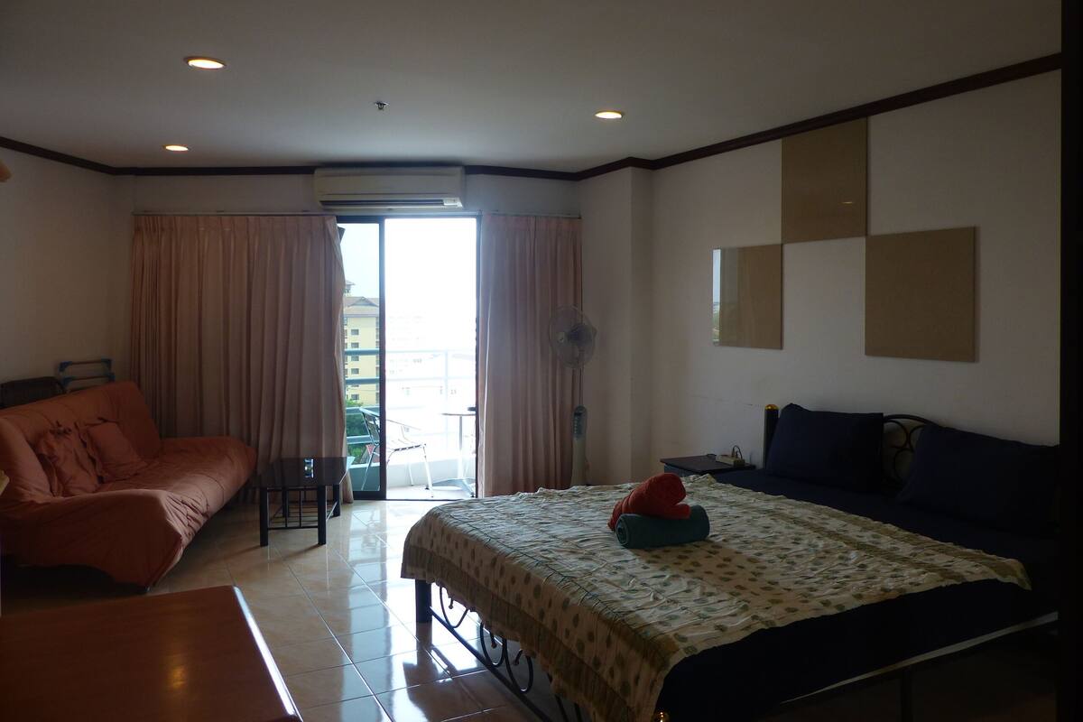 A hotel room with a bed, a sofa, a desk, and a view of the outside.