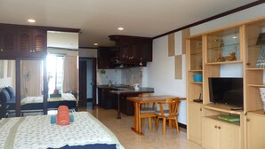 Une pièce comprenant un lit, une table à manger avec des chaises, un coin cuisine et un téléviseur posé sur un meuble en bois.