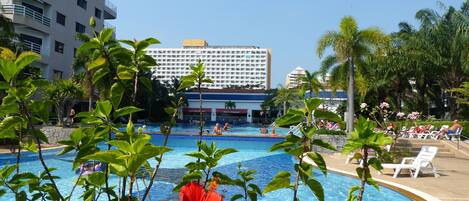 A swimming pool surrounded by lush greenery and a hotel building in the background.