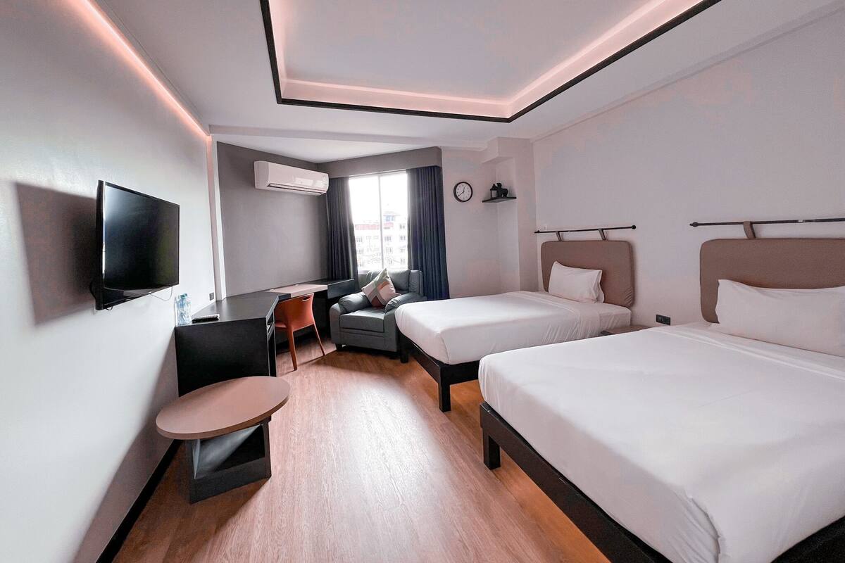 Een moderne hotelkamer met twee bedden, een bureau, een stoel, een televisie en een raam met gordijnen.