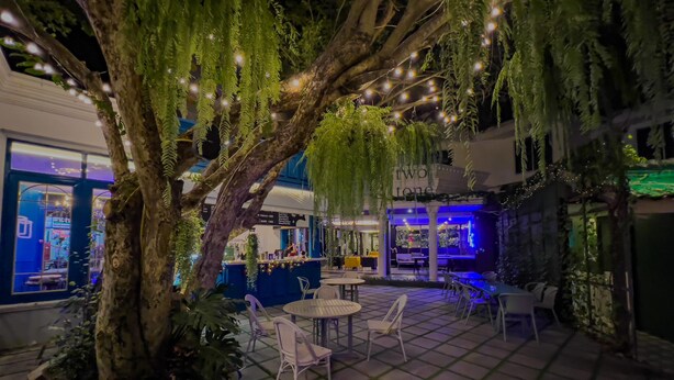 An outdoor patio area with a large tree, seating arrangements, and a bar area. - PRS Hotel by Sojourn (Pattaya)