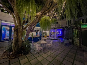 An outdoor patio area with a large tree, seating arrangements, and a bar area.