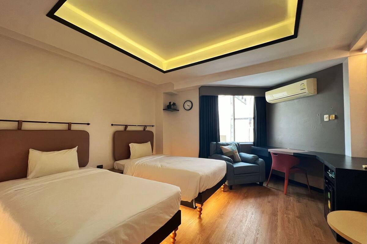 Een hotelkamer met twee bedden, een bureau, een stoel, een klok en een airconditioning.