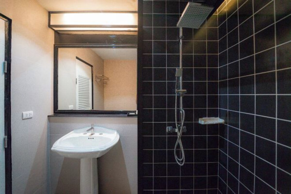 A bathroom with a white sink, a mirror, and a shower with black tiles.