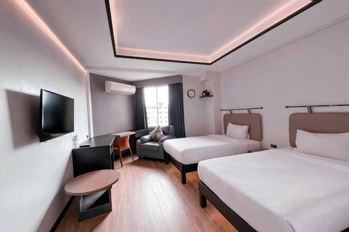 Een moderne hotelkamer met twee bedden, een bureau, een stoel, een televisie en een airconditioning.