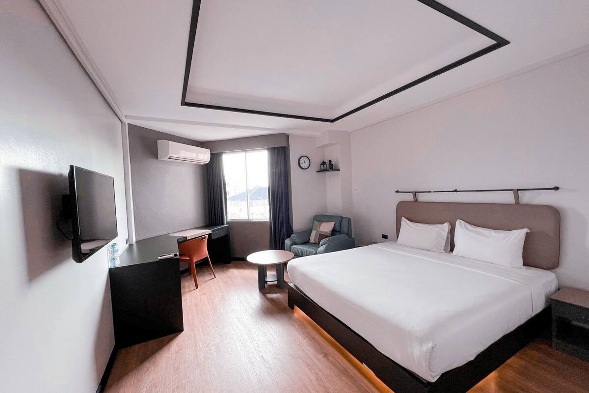 Een hotelkamer met een groot bed, een bureau met stoel, een televisie en een raam met gordijnen.