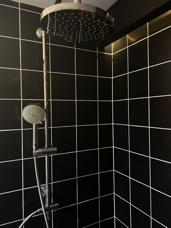 A shower with a handheld showerhead and a fixed wall-mounted showerhead in a tiled bathroom.