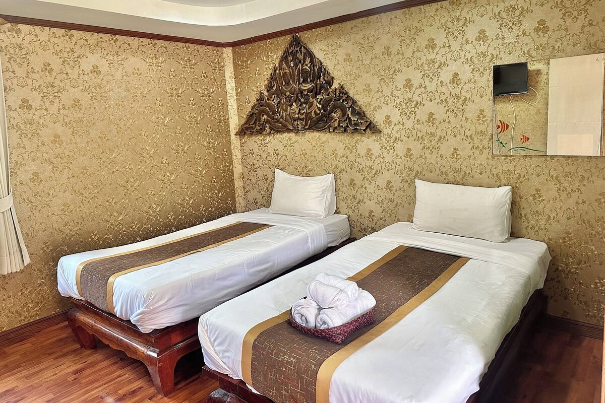 A hotel room with two single beds, a decorative wall piece, a flat-screen TV, and a wooden floor.