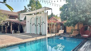 A swimming pool with a wooden deck, a covered seating area, and string lights. - Montri Resort Donmuang Bangkok (Bangkok)