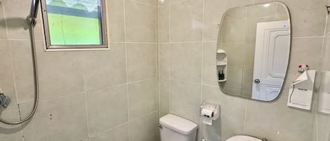 Un baño con inodoro, lavamanos y ducha. Hay una ventana con vista a un campo verde.