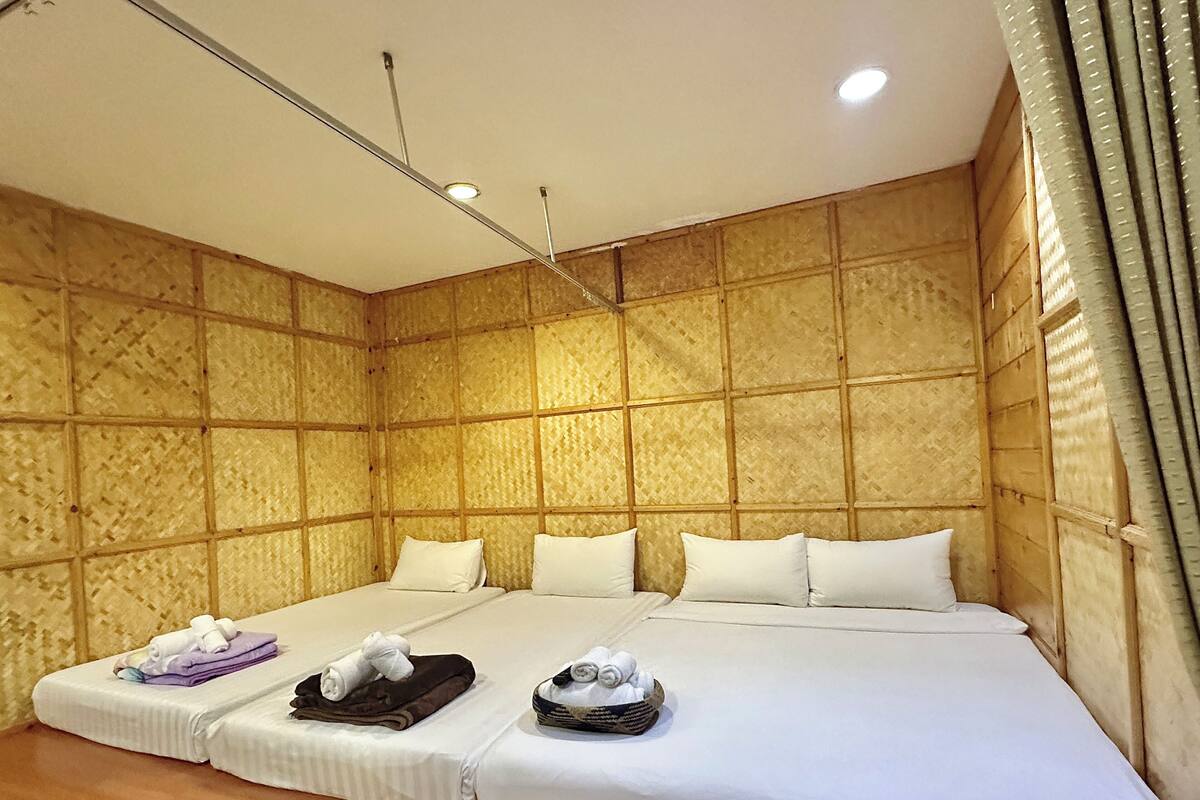 A hotel room with a large bed, two pillows, a small table with towels, and a headboard with a light fixture.