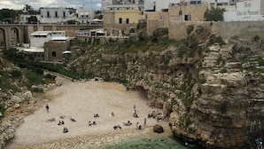 A coastal area with a rocky beach, clear water, and buildings in the background. - B&B Petali Rosa (Polignano a Mare)