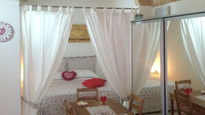A cozy bedroom with a bed under a stone arch, a dining table with chairs, and a mirror reflecting the room. - B&B Petali Rosa (Polignano a Mare)