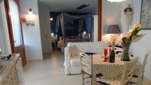 A cozy room with a dining table set for two, a bed with a canopy, and a small table with a vase of flowers. - B&B Petali Rosa (Polignano a Mare)