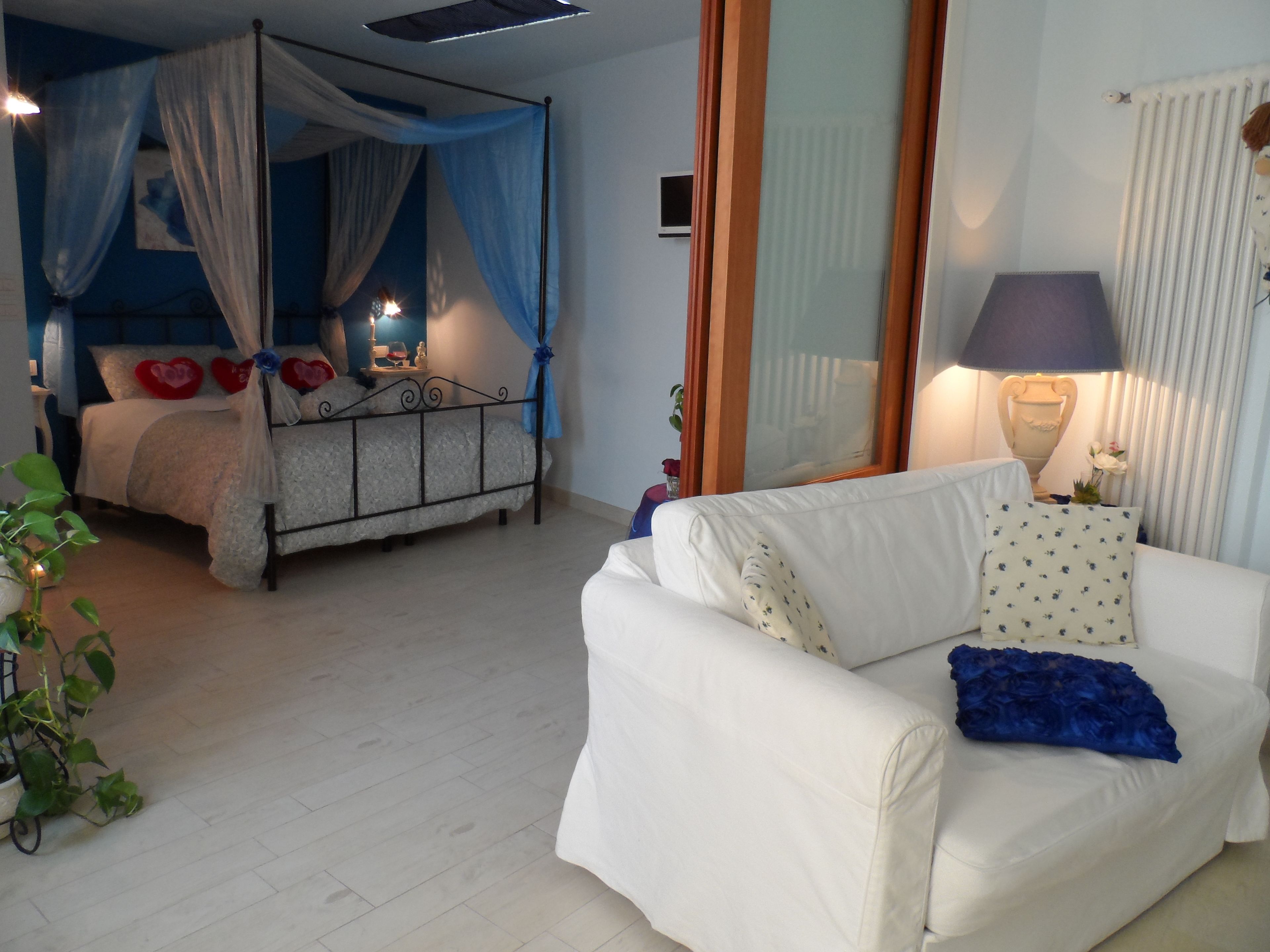 A bedroom with a four-poster bed, a white sofa, and a bedside table with a lamp.
