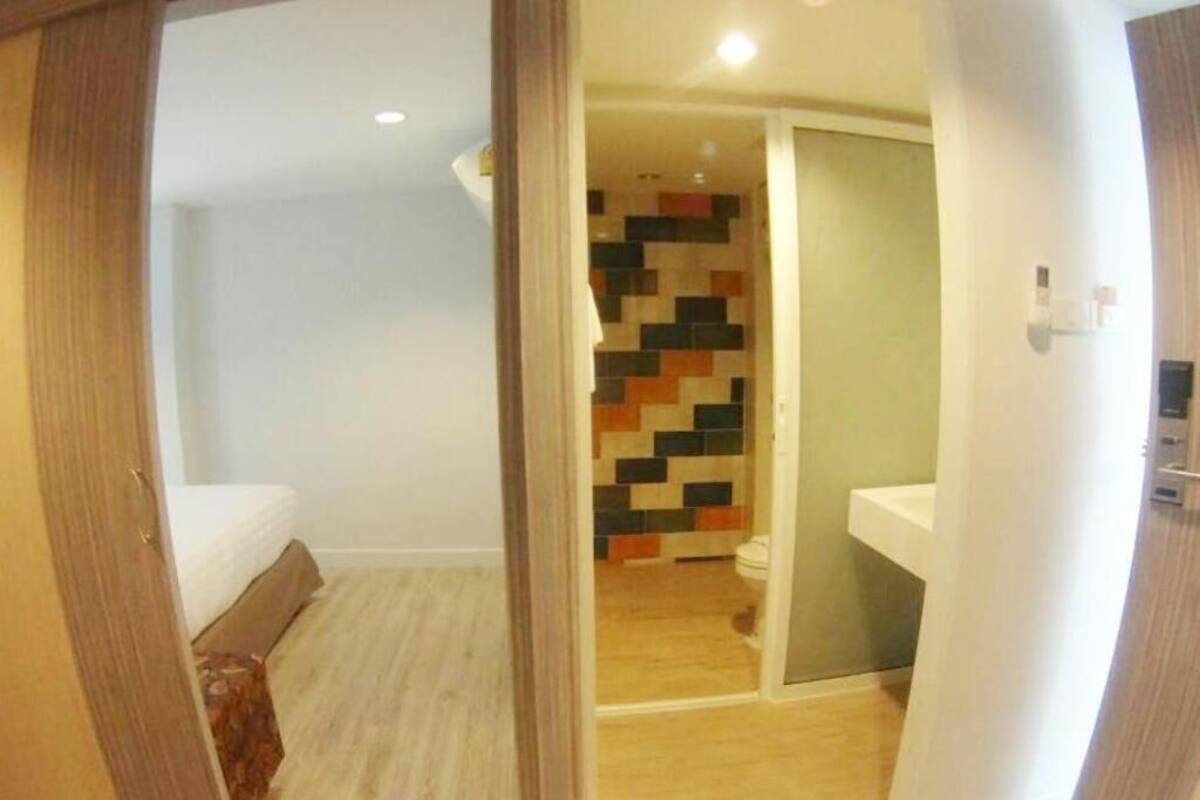 A room with a bed, a bathroom with a tiled wall, and a wooden floor.