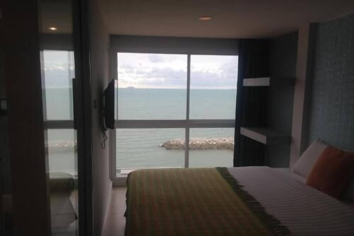 A bedroom with a large window, a bed, and a view of the sea.