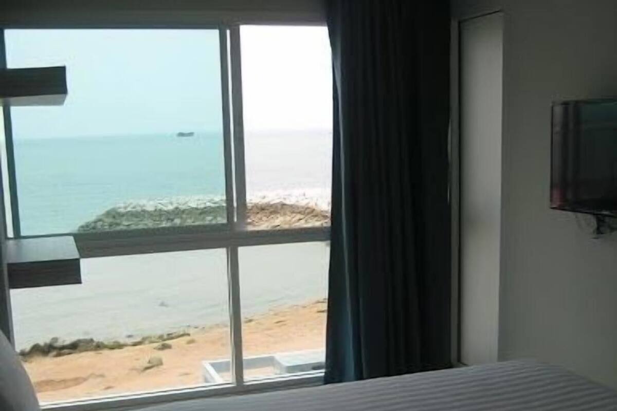 A hotel room with a large window offering a view of the beach and ocean.