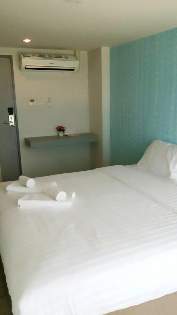 Una cama bien hecha con ropa de cama y toallas blancas, un pequeÃąo estante con un florero, y una pared de acento azul.