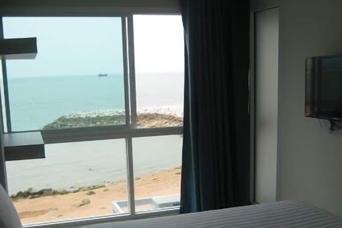 A hotel room with a large window offering a view of the beach and ocean.
