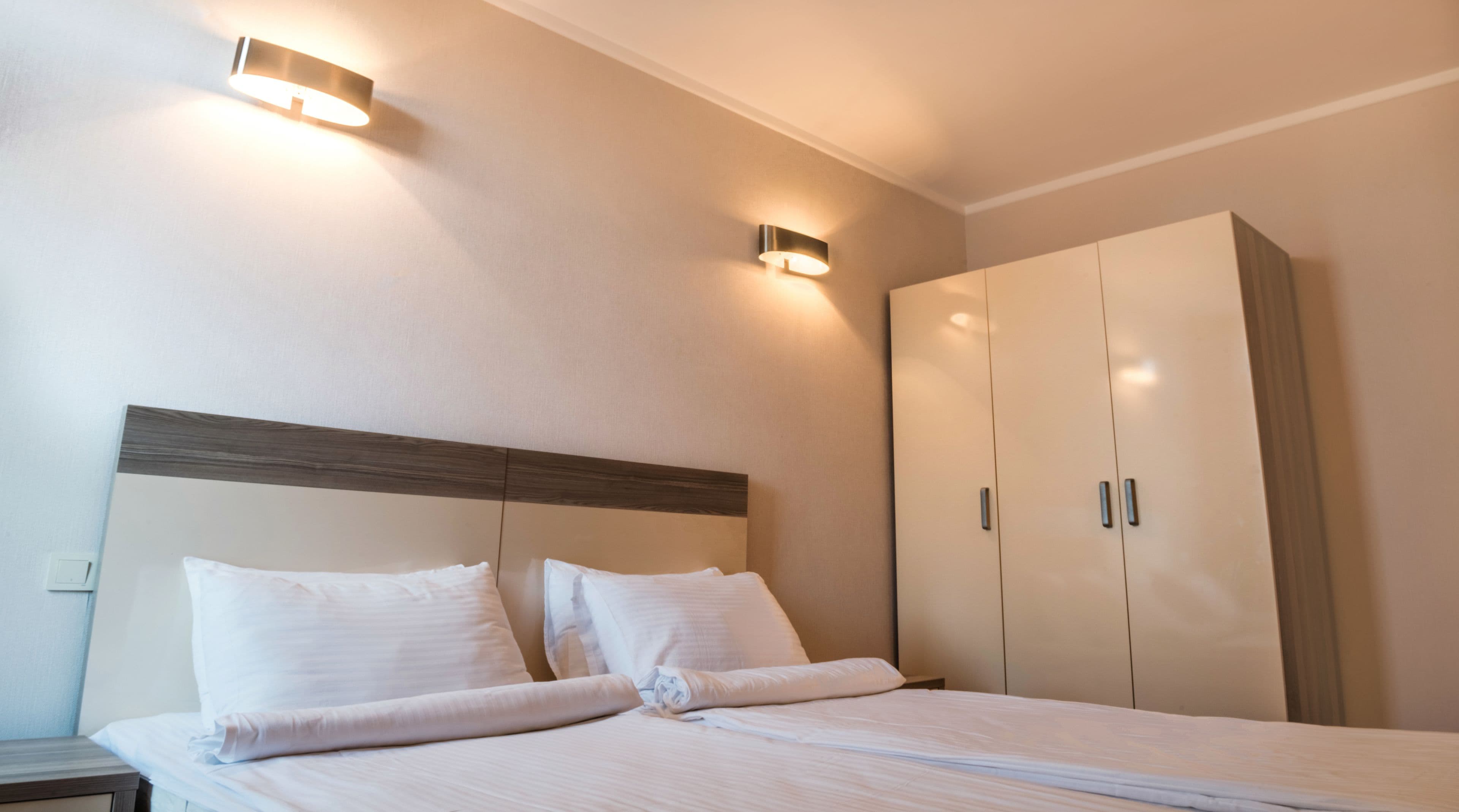 A hotel room with a bed, two bedside tables, a wardrobe, and wall-mounted lighting.